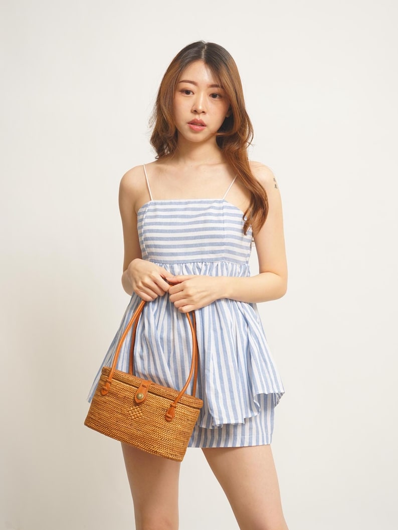 Puede incluir: Conjunto de dos piezas a rayas azules y blancas, con un bolso de mano tejido a juego. El conjunto incluye un top con tirantes finos y un pantal&oacute;n corto. El bolso tiene asas de cuero marr&oacute;n y un cierre.