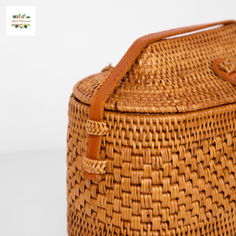 Peut inclure: Sac &agrave; main en rotin tress&eacute; de forme cylindrique avec une poign&eacute;e en cuir. Le sac est de couleur marron clair et pr&eacute;sente une texture tiss&eacute;e. Il est dot&eacute; d'un couvercle et d'une fermeture &agrave; lani&egrave;re en cuir. Style boh&egrave;me naturel.