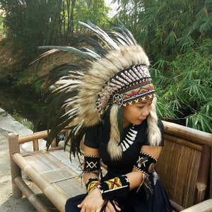 May include: A Native American-style headdress with a brown and tan fur base and tall, dark feathers. The headdress features intricate beadwork in various colors and is worn with matching armbands.