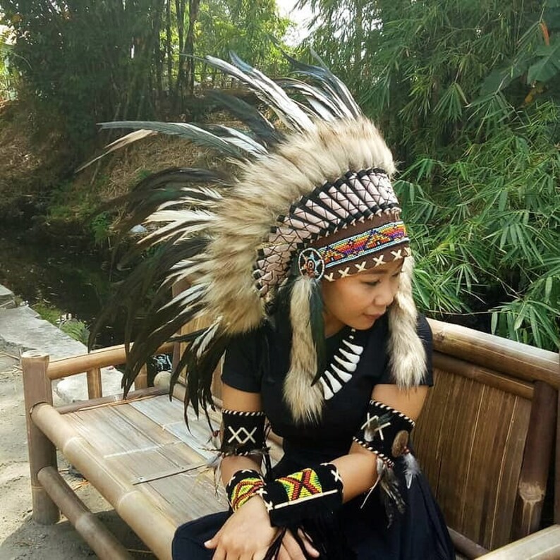 May include: A Native American-style headdress with a brown and tan fur base and tall, dark feathers. The headdress features intricate beadwork in various colors and is worn with matching armbands.