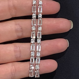 May include: A pair of long silver earrings with a row of clear rectangular and round cubic zirconia stones.