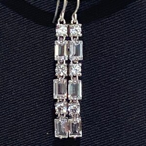 May include: Silver dangle earrings with multiple clear crystal stones in a rectangular and round shape.