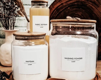 May include: Three glass jars with bamboo lids and labels on a wooden tray. The labels read "Fabric Softener", "Washing Powder", and "Napisan".