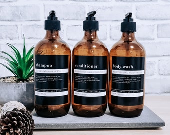 Può includere: Tre bottiglie di vetro ambrato con etichette nere e testo bianco. Le bottiglie sono etichettate "shampoo", "balsamo" e "doccia schiuma". Ogni bottiglia contiene 8 oz di prodotto.