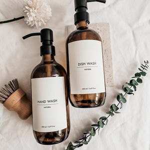 Pu&ograve; includere: Due flaconi in vetro ambrato con pompe nere, etichettati "HAND WASH" e "DISH WASH" in stile minimalista. Ogni flacone contiene 500 ml. Una spazzola di legno e del verde suggeriscono un tema naturale ed ecologico.