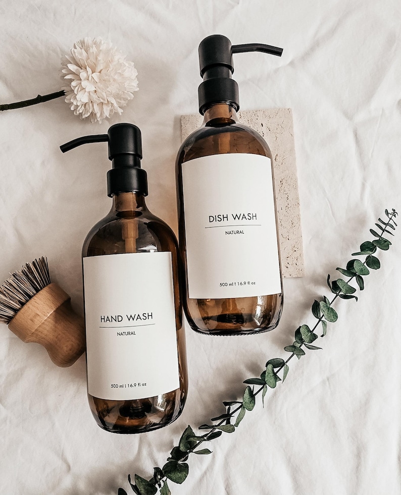 Pu&ograve; includere: Due flaconi in vetro ambrato con pompe nere, etichettati "HAND WASH" e "DISH WASH" in stile minimalista. Ogni flacone contiene 500 ml. Una spazzola di legno e del verde suggeriscono un tema naturale ed ecologico.