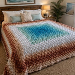 Könnte beinhalten: Eine Häkeldecke mit quadratischem Muster und Farbverlauf. Die Mitte ist in leuchtendem Türkis gehalten, geht nach außen in helle Grün-, Weiß- und Beigetöne über und endet in einem dunkelbraunen Rand mit einer strukturierten Maschenoptik.