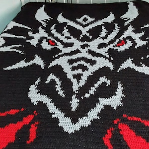 May include: A black and gray crocheted blanket with a dragon design. The dragon's eyes are red.