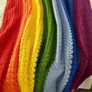 May include: A rainbow crochet blanket with a textured stitch pattern. The blanket is made in the colours red, orange, yellow, green, blue, and purple.