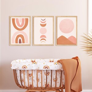 Puede incluir: Un moisés de mimbre con una sábana estampada en blanco y naranja, una manta marrón y una alfombra tejida. El moisés está en una habitación de bebé con tres impresiones de arte abstracto en la pared.