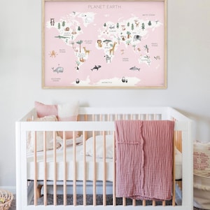 May include: A pink and white world map with animal illustrations and the text "PLANET EARTH" printed on it. The map is framed in a light wood frame and is hanging on a white wall above a white crib with a pink blanket.