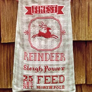 May include: A gray sack with red text and a reindeer graphic. The text reads "FINEST REINDEER Sleigh Power 25 LBS NET FEED NORTH POLE". The reindeer graphic is inside a red framed design with snowflakes.