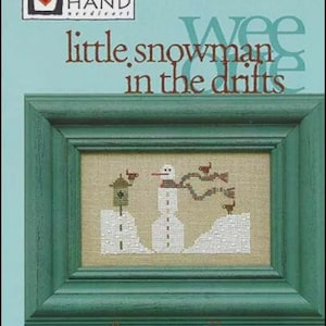 May include: A framed cross-stitch design titled "little snowman in the drifts." The artwork features a snowman, a birdhouse, and birds, all rendered in white and brown thread on a beige background. The frame is a teal green color.