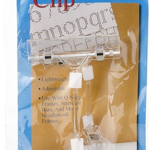 May include: Clear plastic Chart Clip for needlework projects. The packaging features the text "Chart Clip" in red, with product features listed as lightweight and adjustable. It is designed to be used with Q-Snap frames and other needlework frames.