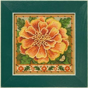 May include: A framed cross-stitch embroidery featuring a large, vibrant orange and yellow marigold flower centered on a tan grid fabric. The design includes green leaves, a small butterfly in the lower right, and a decorative floral border.