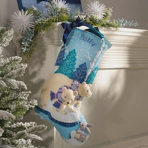 May include: A light blue Christmas stocking with a winter scene featuring polar bears and a rabbit. The stocking is decorated with embroidered trees and snowflakes. The name "Sally" is embroidered on the top.