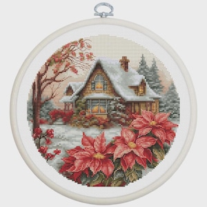 May include: A cross-stitch embroidery in a round hoop depicts a snow-covered house with a warm glow from the windows. Red poinsettias bloom in the foreground. The scene is set in a winter landscape with trees and a muted color palette.