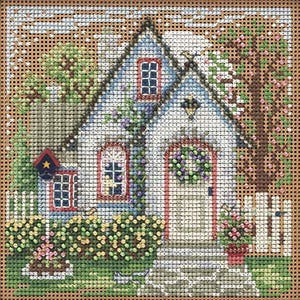May include: A cross-stitch design of a quaint cottage with a blue roof, red-trimmed windows, and a white picket fence. The cottage is adorned with a floral wreath and surrounded by lush greenery and flowering trees, creating a charming, idyllic scene.