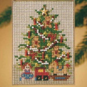 May include: A cross-stitch embroidery on a light fabric featuring a green Christmas tree decorated with red candles, white garlands, small yellow stars, and gingerbread figures. At the base of the tree are a doll, a red toy train, and a rocking horse.