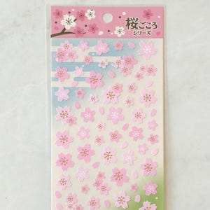 May include: A sheet of pink and white cherry blossom stickers with the text "桜ごころ" (Sakura Gokoro) and "シリーズ" (Series) in Japanese. The stickers are perfect for adding a touch of spring to your crafts and projects.