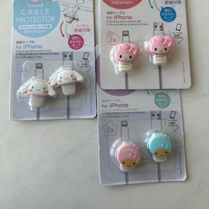 May include: Two packages of cable protectors for iPhone charging cables. Each package features a different cartoon character, one with a pink and white design and the other with a blue and white design. The packages include two cable protectors each.