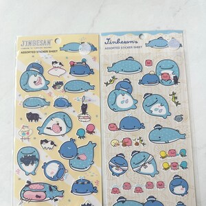 May include: Two sheets of assorted stickers featuring whale illustrations. The stickers are on a yellow background with a white border. The text "Jinbesan" and "Assorted Sticker Sheet" is printed on each sheet.