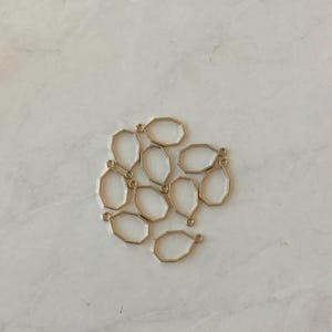 May include: A group of ten gold-toned metal octagon-shaped pendant blanks with a loop at the top.