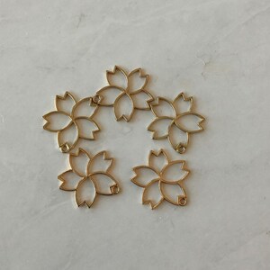 May include: Five gold metal flower-shaped charms with a loop at the top of each charm.