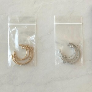 May include: Two clear plastic bags containing three gold and three silver crescent moon shaped metal charms.