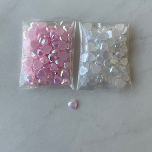 May include: Two bags of iridescent heart-shaped embellishments. One bag contains pink hearts, and the other contains white hearts.