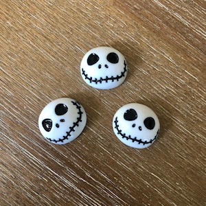 May include: Three white ceramic buttons with a black Jack Skellington face design. The buttons are round and have a stitched mouth.