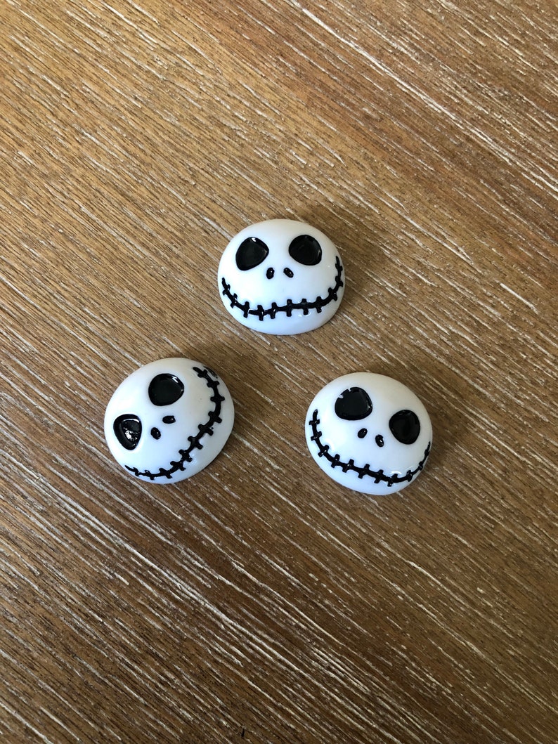 Puede incluir: Tres botones de cer&aacute;mica blanca con un dise&ntilde;o de cara negra de Jack Skellington. Los botones son redondos y tienen una boca cosida.