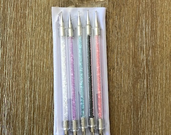 May include: Set of five nail art tools with different shaped tips. The tools are clear with glitter accents in various colors, including white, purple, blue, black, and pink.