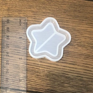 May include: A white silicone mold shaped like a star with a smaller star inside. The mold is about 2 inches in diameter.