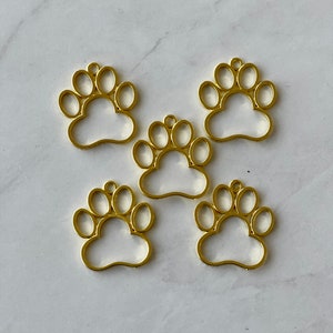 May include: Five gold-colored metal paw print charms with a hole at the top for hanging.