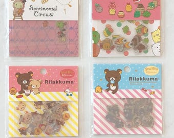May include: Four packages of clear sticker sheets with various cartoon characters. The stickers are on a pink and yellow background. The packages are labeled "Sentimental Circus", "Rilakkuma", and "Rilakkuma".
