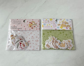 May include: Two packages of stickers featuring adorable cartoon animals. The stickers are on a pink and green background with white polka dots. The text on the packages reads "Coro coro coronya" and "Stickers Autocollants".