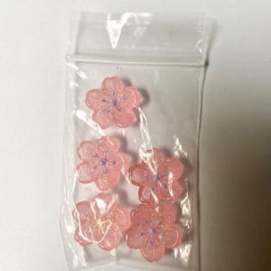 May include: Five pink and white glass cherry blossom flower charms with blue accents. The charms are in a clear plastic bag.