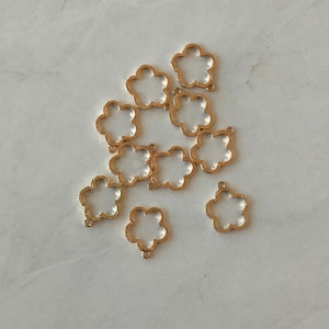 May include: Ten gold metal flower-shaped charms with a hole at the top for attaching to jewelry or other crafts.
