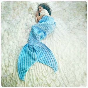 May include: A light blue mermaid tail blanket with a textured, bubble-like pattern. The tail is curled up on a white surface.