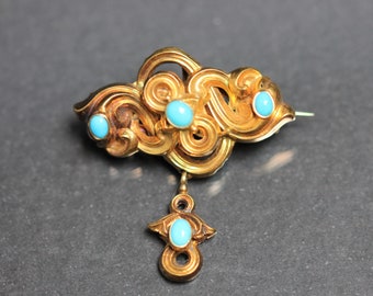 May include: A gold brooch with a swirling design and four turquoise stones. The brooch has a dangling pendant with a turquoise stone.