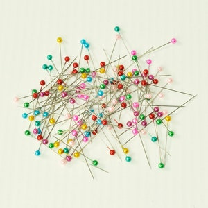 May include: A large pile of colorful sewing pins with silver metal shafts and colored plastic heads. The colors include red, blue, green, yellow, and pink.