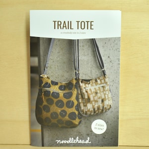 Puede incluir: Un folleto titulado "TRAIL TOTE" presenta dos bolsos cruzados. Uno es amarillo mostaza con patrones de círculos negros, el otro es beige con un diseño geométrico blanco. El texto "2 sizes to sew!" también es visible.