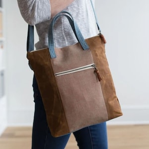May include: A brown, canvas tote bag with a blue strap and a zippered pocket. The bag has a brown leather trim and a tassel.