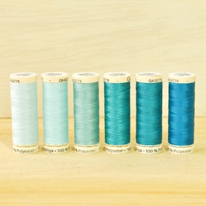 May include: Seven spools of thread in various shades of blue, from light blue to teal. Each spool is labeled with the text "100% Polyester" and a product code.