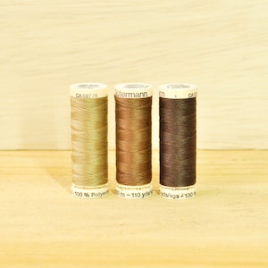 May include: Three spools of thread in different shades of brown. The spools are labeled with the brand name "Gütermann" and the text "100% Polyester 110 yds/100 m".