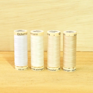 May include: Four spools of white thread, each with a different shade of white. The spools are labeled with the brand name "Gutermann" and the length of the thread in yards and meters.