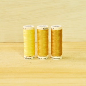 May include: Three spools of yellow thread, from lightest to darkest, with labels that read "Gutermann", "100 m", and "Polyester".
