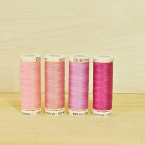 May include: Four spools of Gutermann thread in shades of pink, ranging from light to deep magenta. Each spool is labeled with the brand name and the amount of thread, 100 yds/vgs.