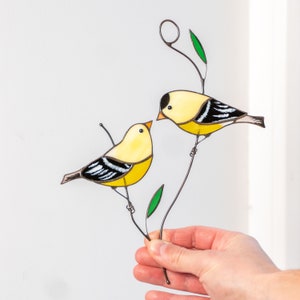 Goldfinches sitting on the wire branch with green leafs stained glass window hangings